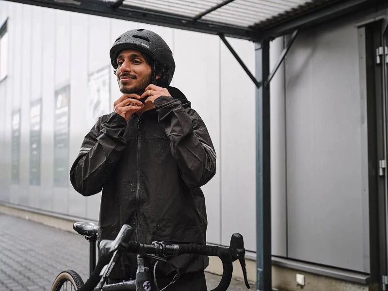 Ein Mann mit Regenmantel zieht sich einen schwarzen Helm auf und steigt auf sein Fahrrad Ein Mann mit Regenmantel zieht sich einen schwarzen Helm auf und steigt auf sein Fahrrad