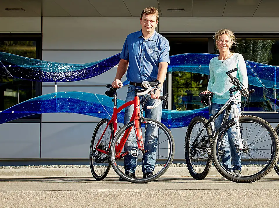 Zwei glückliche Menschen stehen mit ihrem JobRad vor dem Endress und Hauser Gebäude Zwei glückliche Menschen stehen mit ihrem JobRad vor dem Endress und Hauser Gebäude